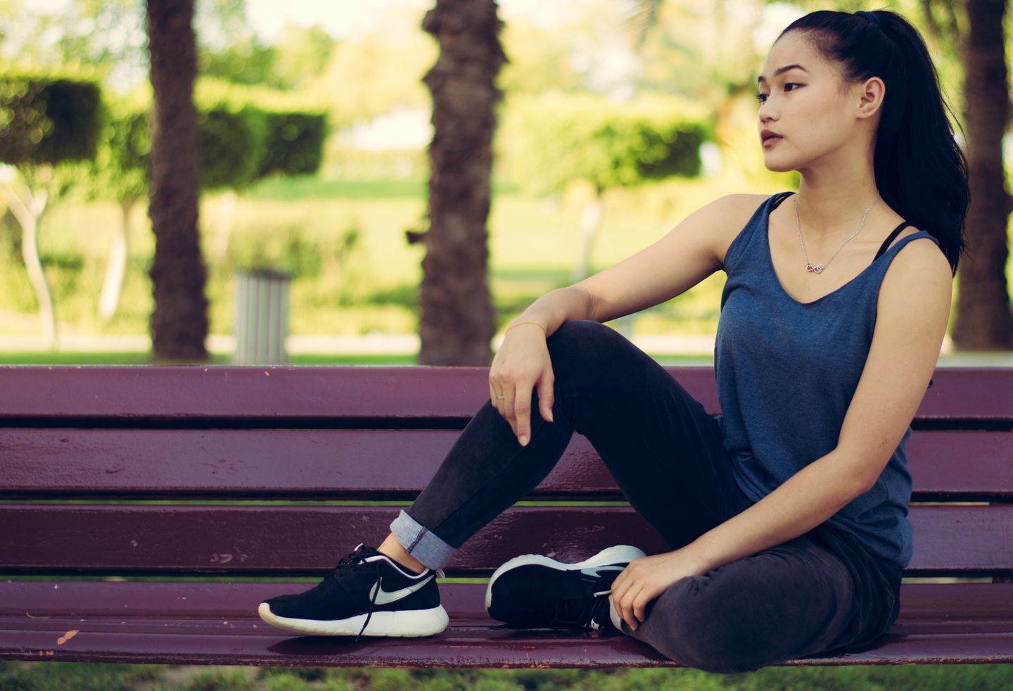 A young woman sits gracefully on a park bench, embodying tranquility and style.
